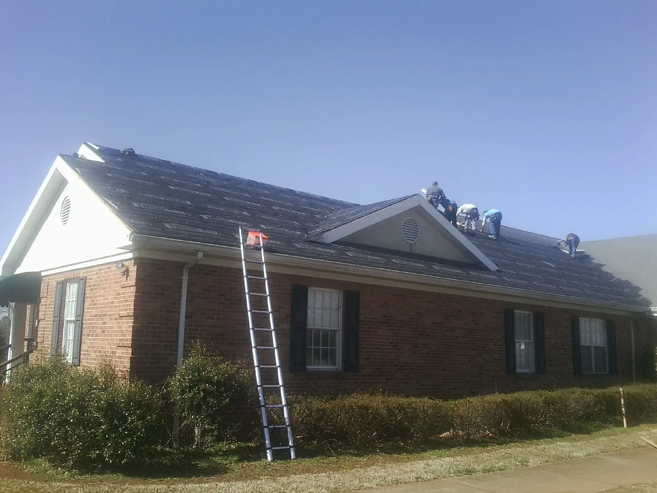 Crew tearing shingles off a brick ranch roof with a ladder set — Emergency Roof Repair work by our crew in Tekamah