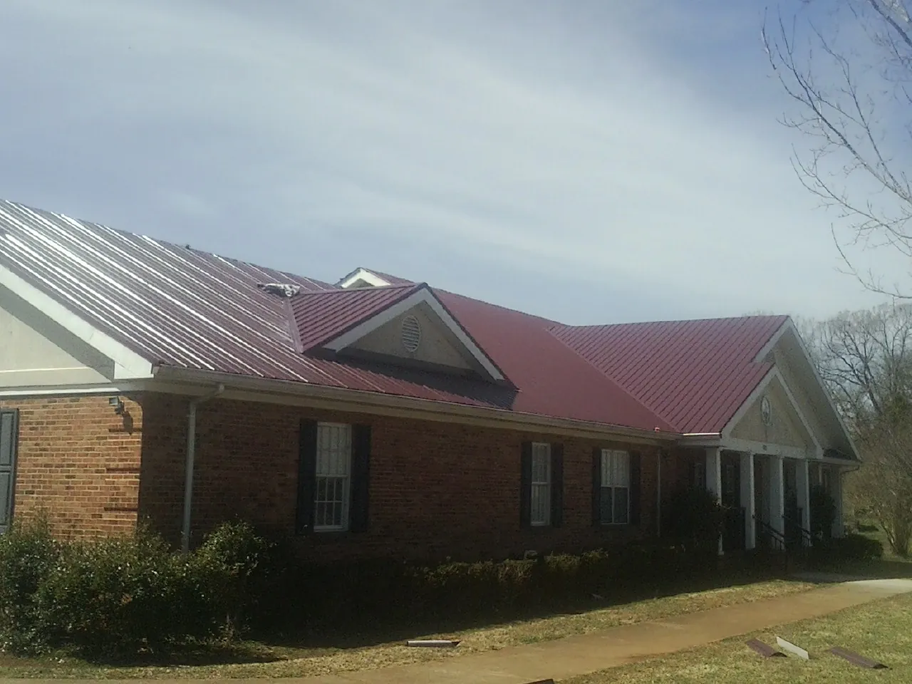 Red metal roof with gabled entries on a long brick building, from a Hail Damage Roof Repair job in Tekamah