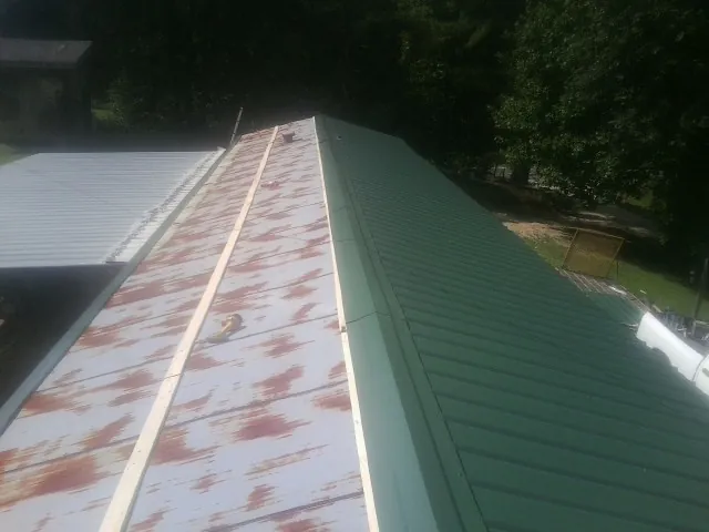 Old rusted panels beside newly installed green metal roofing — Wind Damage Roof Repair by Roofing Brothers in Tekamah