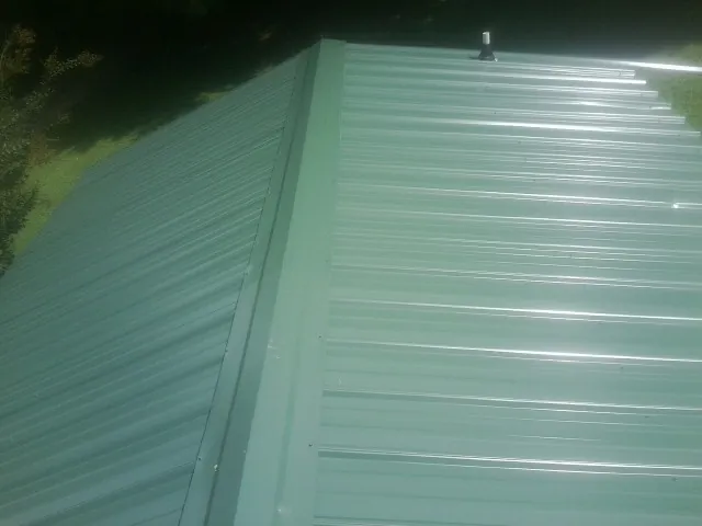 New green metal panels meeting at the ridge of a roof — Flat Roof Repair work by our crew in Tekamah