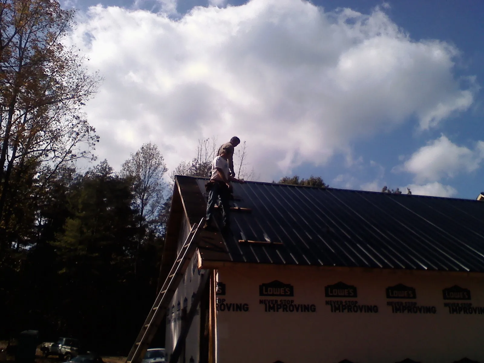 Roofer fastening dark metal panels high against a cloudy sky, from a Roof Inspection job in Tekamah