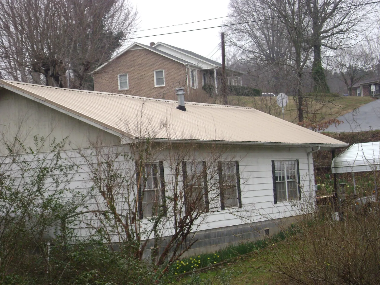 Tan metal roof on a white sided house set into a hillside — Commercial Roofing by Roofing Brothers in Tekamah